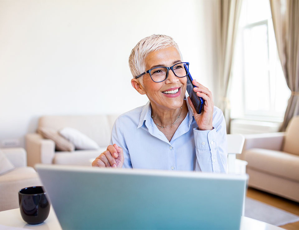 happy new patient talking on the phone with a computer in front of her